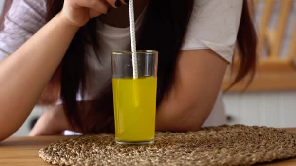 Close up, young woman drinking orange soda in kitchen. Female enjoying carbonated lemonade sipping through straw. - Filmagem, Vídeo