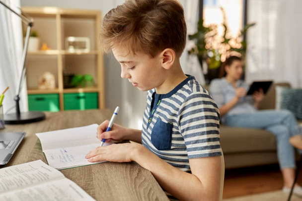 student boy with book writing to notebook at home - Foto, Bild
