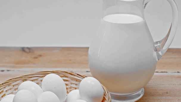 Яйця в кошику і глек з молоком на дерев "яній поверхні ізольовані на сірій. - Кадри, відео