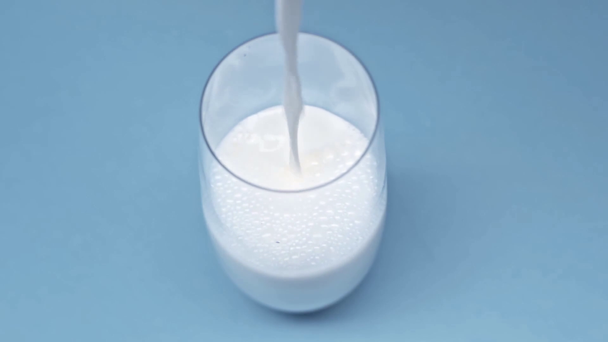 Высокий угол обзора налива молока в стекло на голубую поверхность
 - Кадры, видео
