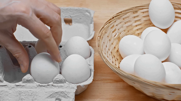 Vista ritagliata dell'uomo che mette le uova dal cesto di vimini nella scatola sulla superficie di legno
 - Filmati, video