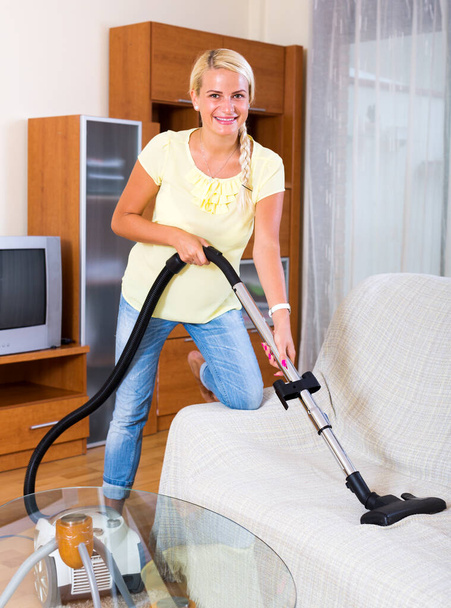 Positive young woman hoovering in living room and smiling - Fotografie, Obrázek