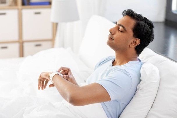 happy indian man with smart watch in bed at home - Valokuva, kuva