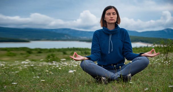 Eine junge Frau macht Yoga auf dem Feld. Sensibilität für die Natur. Selbstanalyse und Gewissenserforschung. Spirituelles und emotionales Konzept. - Foto, Bild