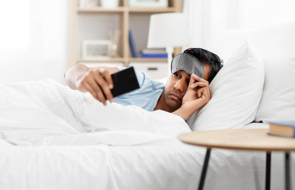sleepy indian man with smartphone lying in bed - Foto, Imagem