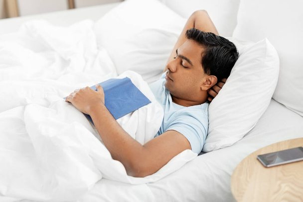 indian man with book sleeping in bed at home - Foto, afbeelding