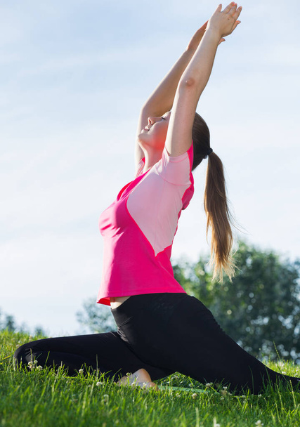 Smiling adult female in pink T-shirt is practicing stretching in the park. - Foto, afbeelding
