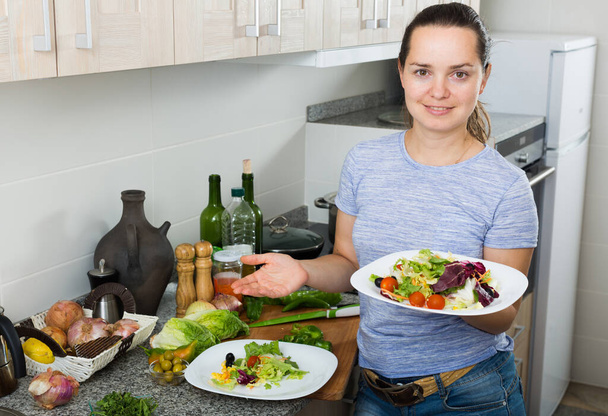 Portrait of smiling young woman serving fresh healthy salad indoors in apartment - Fotó, kép