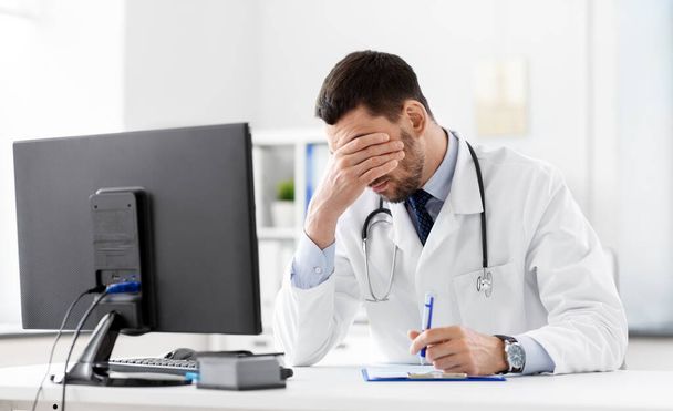 stressed male doctor with clipboard at hospital - Foto, afbeelding