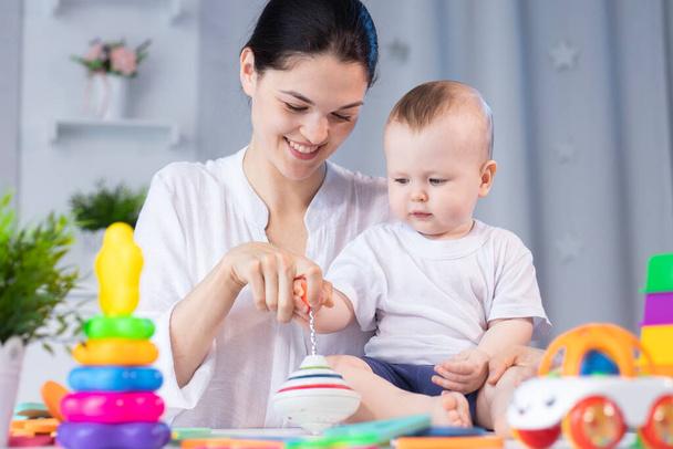 Mom and little son are playing with different developing toys in a bright children's room - Foto, imagen