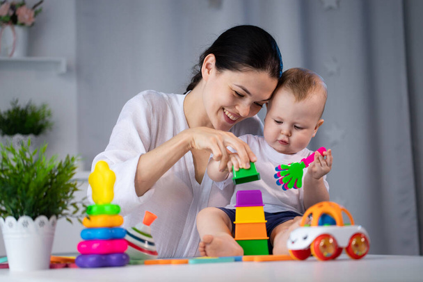 Mom and little son are playing with different developing toys in a bright children's room - Foto, afbeelding