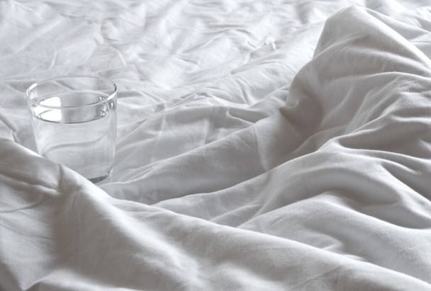 A glass of water on the blanket crumpled on the bed - Photo, Image