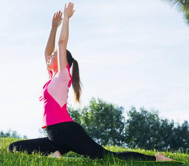 Adult woman in pink T-shirt is practicing stretching in the park. - Photo, image