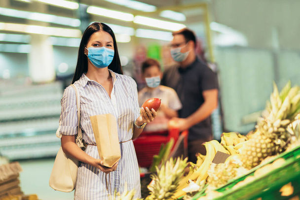 Happy family wearing face protective medical masks for protection from virus disease with shopping cart buying food at supermarket. New normal. - Photo, Image
