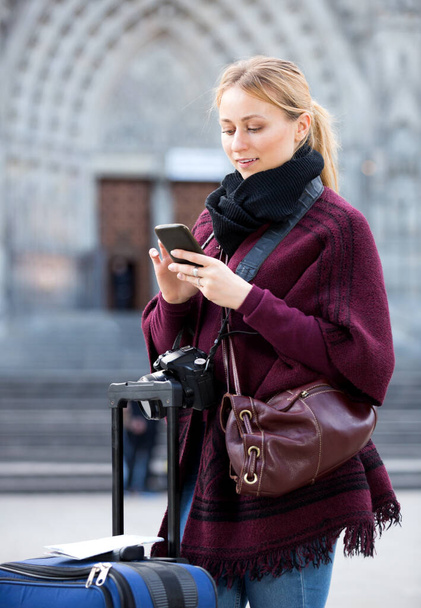 Blond smiling young girl holding phone in hands and looking up her way using app, gps - Zdjęcie, obraz