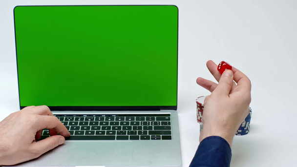 καλλιεργημένη άποψη του ανθρώπου χρησιμοποιώντας φορητό υπολογιστή με πράσινη οθόνη και κρατώντας ζάρια σε λευκό - Πλάνα, βίντεο