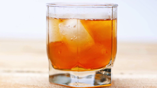 Glas Whisky mit Eiswürfeln auf Holztisch isoliert auf weiß - Filmmaterial, Video