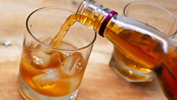 zpomalený pohyb whisky nalévající se z láhve do skla s kostkami ledu  - Záběry, video