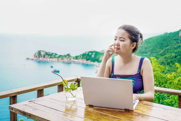 Asiatique jeune femme travaillant en ligne heureux avec fond de vue sur la mer depuis le balcon au-dessus de la hauteur du niveau de la mer
 - Photo, image