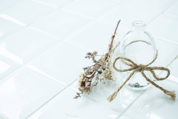 Empty transparent vintage bottle with rope and dried flower on white dining table - Фото, изображение