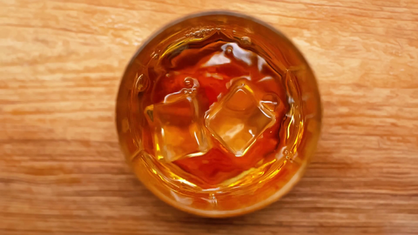 a jégkockák lassított mozgása a fából készült asztalra hulló whisky üvegébe - Felvétel, videó