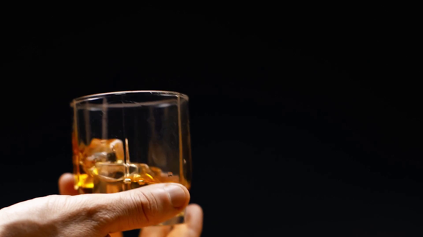 male hand with glass of whiskey and ice cubes isolated on black, slow motion - Footage, Video