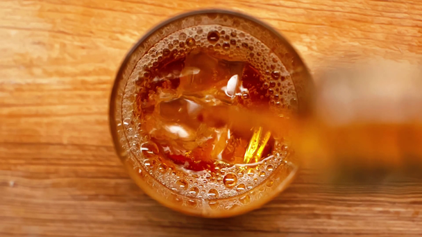 木製のテーブルの上に氷のキューブでガラスに注ぐウイスキーのトップビュー - 映像、動画