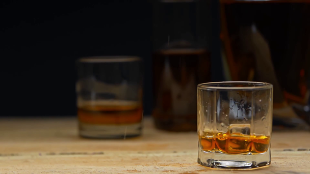 a jégkocka lassított mozgása a fekete whiskey üvegébe hullik - Felvétel, videó