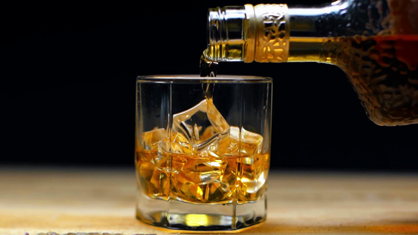 a palackból üvegbe öntött whisky, fekete alapon izolált jégkockákkal - Felvétel, videó