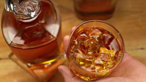oříznutý pohled na muže, jak nalévá whisky do skla poblíž karafy na dřevěném stole - Záběry, video