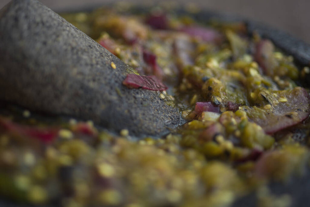 tigela de pedra com moagem de vários alimentos, especiarias, salsas e guacamole - Foto, Imagem