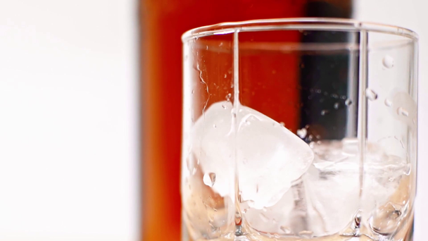 ice cubes falling into glass near bottle of whiskey isolated on white - Footage, Video