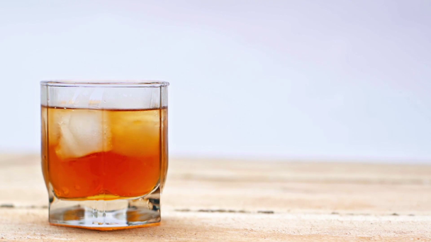glass of whiskey with ices cubes on wooden table isolated on white - Footage, Video