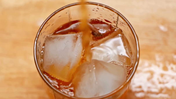 felső kilátás whisky áramlik az üvegbe, jégkockákkal a fa asztalon - Felvétel, videó