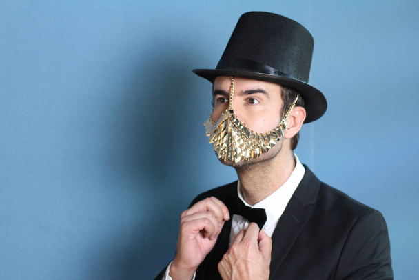 close-up portrait of handsome young man in suit with bow tie, cylinder and fashionable golden mask - Photo, Image