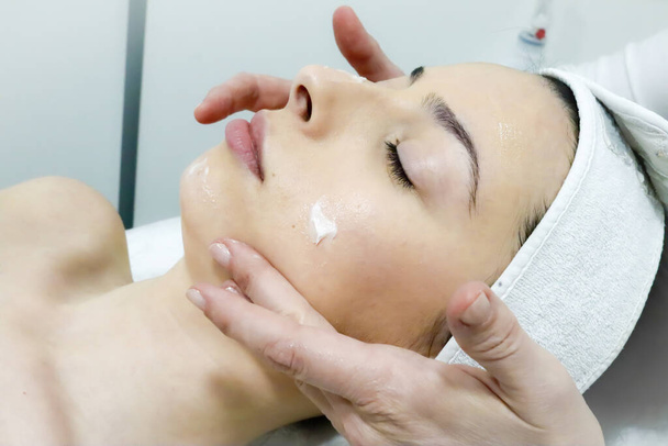 trabalhador esteticista massageia suavemente o rosto do cliente feminino com creme especial no salão de beleza, close-up
 - Foto, Imagem