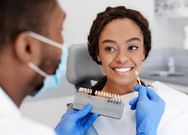 Schwarzer Arzt hält Zahnwaage-Probe über lächelnde junge Frau - Foto, Bild