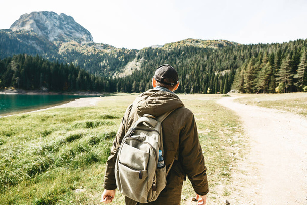 Turysta z plecakiem spaceruje wiejską drogą na tle pięknego krajobrazu w Czarnogórze. - Zdjęcie, obraz
