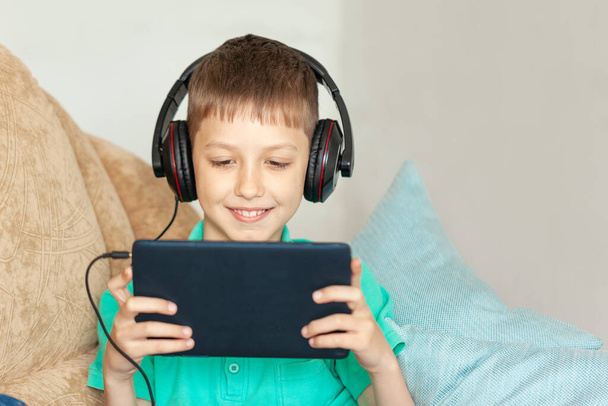 Chłopiec korzystający z tabletu cyfrowego i słuchawek. Kid studiuje z domu i gra w gry wideo z gadżet - Zdjęcie, obraz