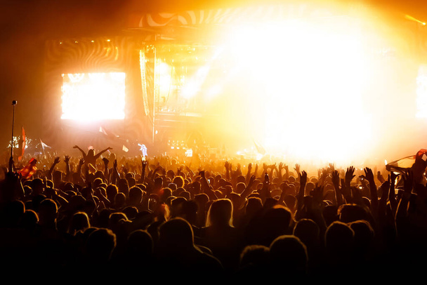Handen omhoog ter ere van een muzikale show op het podium, Mensen in de hal. Oranje licht - Foto, afbeelding