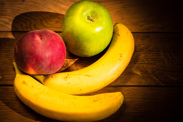 Mela, pesca e banane su una tavola di legno. Composizione di frutti salutari
. - Foto, immagini