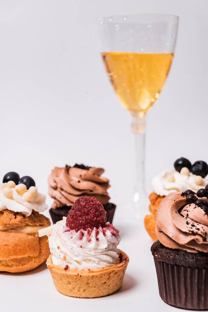 A vertical shot of delicious cupcakes with berries and chocolate on the table with a glass of champagne - Zdjęcie, obraz
