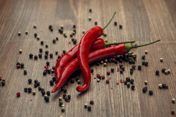 Three red ripe fruits of chili pepper and peppercorns on a wooden background - Photo, Image