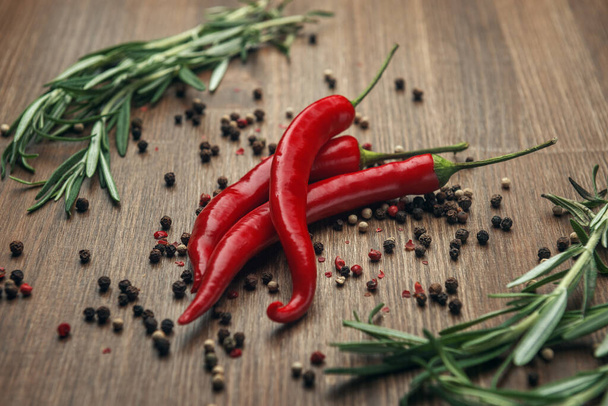 Red ripe fruits of chili pepper with peppercorns and rosemary on a wooden background - Foto, afbeelding