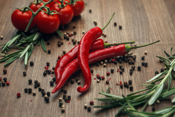 Red ripe fruits of chili pepper and cherry tomato with peppercorns and rosemary on a wooden background - Foto, afbeelding