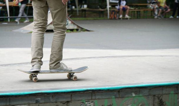 A person playing with a skateboard in a park with some people sitting on the benches - Photo, image