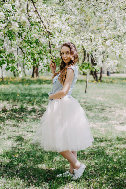 The beautiful girl the blonde holds with eyes closed in hand the blossoming apple-tree branch with white flowers in a garden in sunshine. Spring apple trees in blossom. woman among spring blossom. - Photo, image