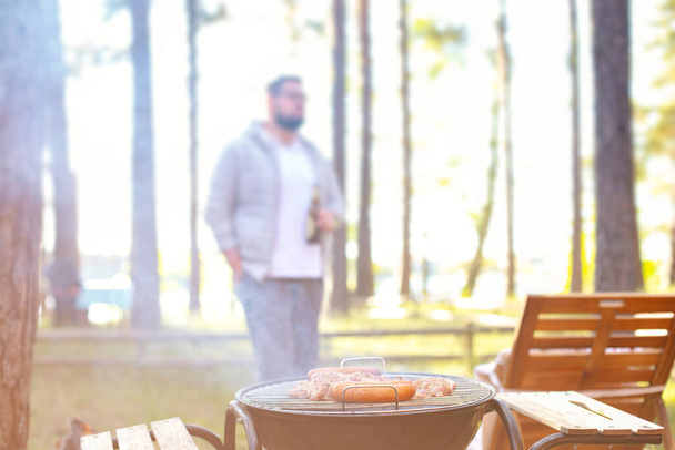 Man standing with beer, cooking meat on a barbecue grill at outdoor summer party. - Photo, Image