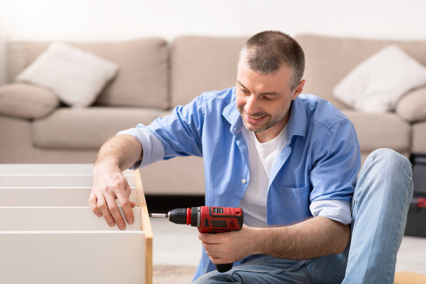 Homem que fixa a mobília que repara o armário usando a broca elétrica em casa
 - Foto, Imagem