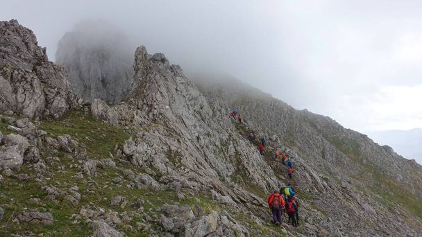 The hikers climbing a rock covered in the fog under a cloudy sky at daytime - Photo, Image